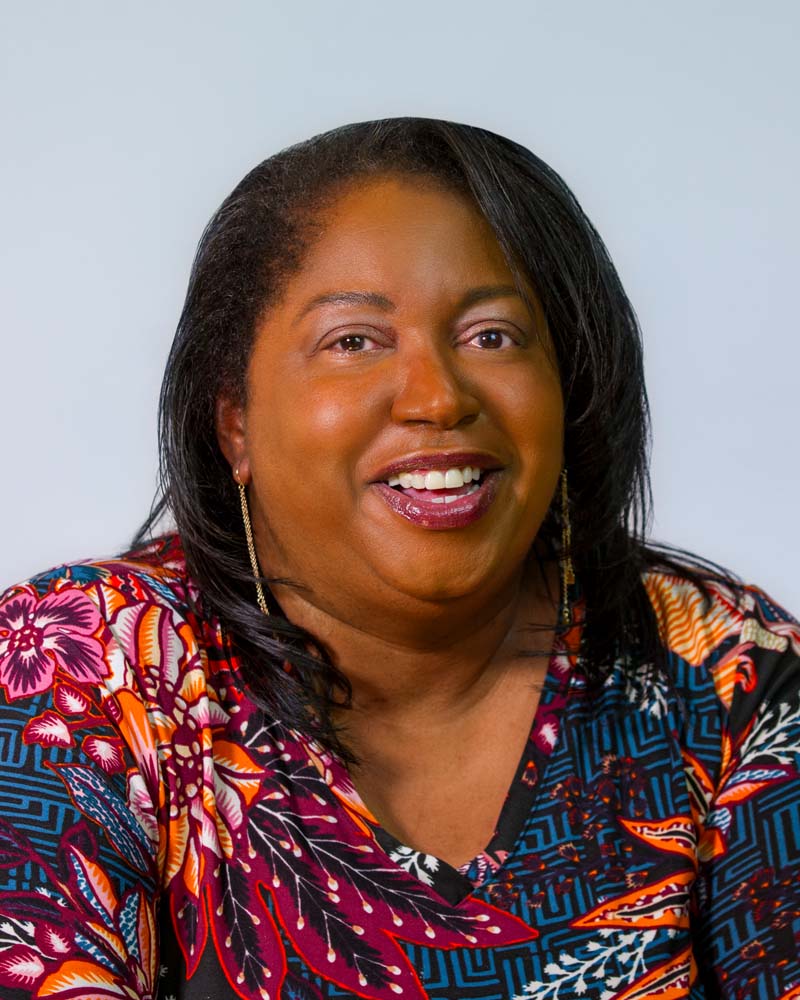 Image: Headshot of Cheryl Mitchell, a black woman with a blue blazer and long golden earings.