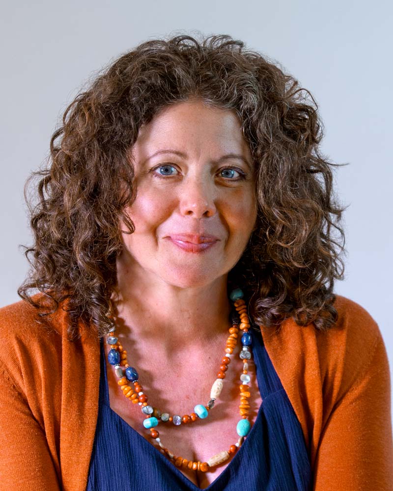 Image: Circular cropped headshot of Heather Evans, a white woman with curly, brown, shoulder length hair & blue eyes, wearing a white button down shirt and a necklace.