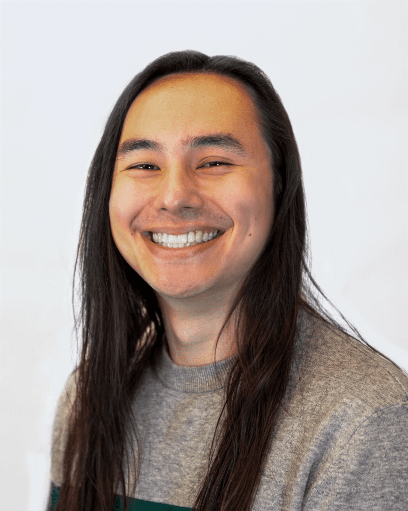 A headshot photo of Cameron smiling at the camera with light grey background.