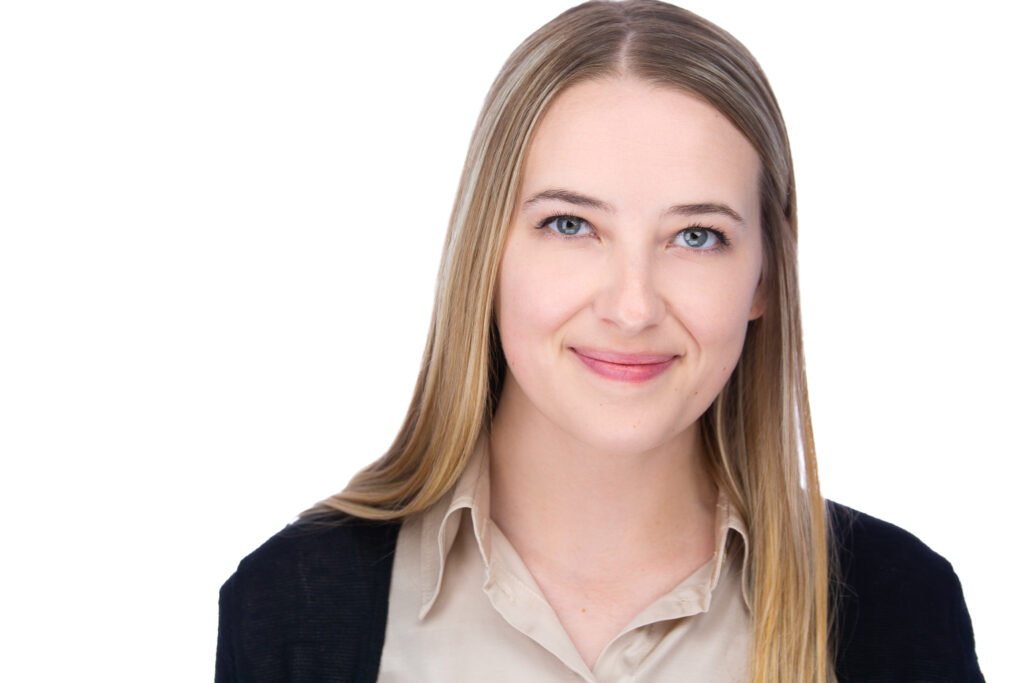 Middle Aged Blonde lady, wearing a tan collared shirt with a black sweater.
