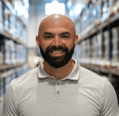 Caucasian man with mustache and beard with a warehouse in the background.