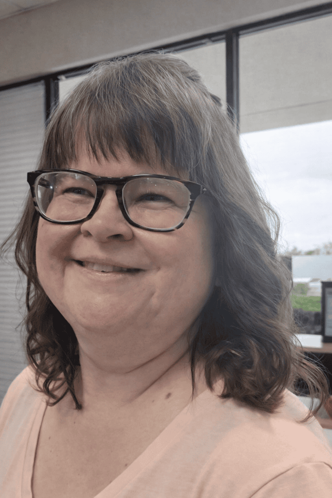Brunette woman with glasses smiling in front of a window