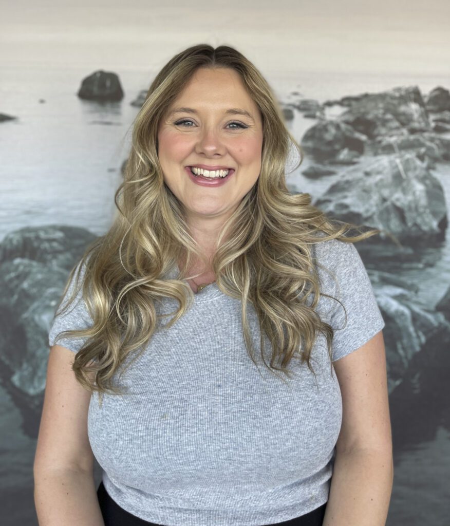 Blonde woman smiling in front of a blue, gray background
