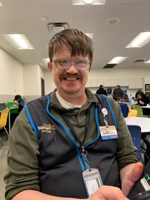 A photo of a man wearing glasses and a Walmart jacket smiling at the camera.
