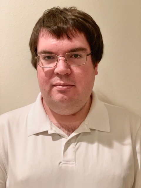 White Male in His 40s, wearing a white polo against a white painted background.