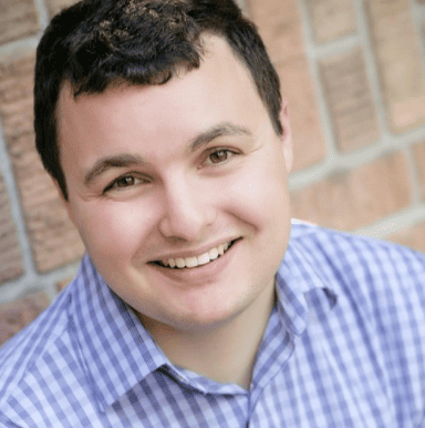 Daniel smiling at the camera against a light red background